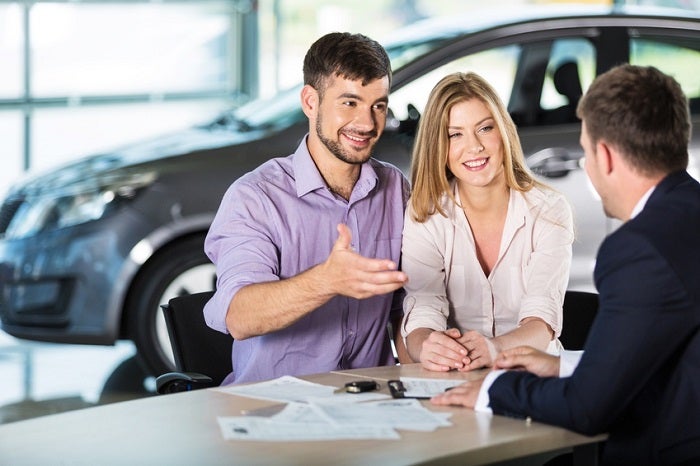 Image of a young couple talking to a car salesman.