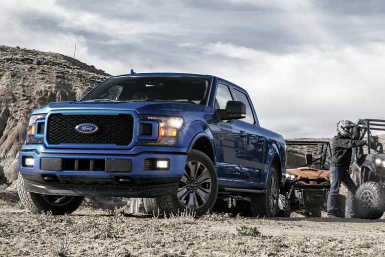 Image of a blue 2019 Ford F-150 driving on a dirt road with mountains.