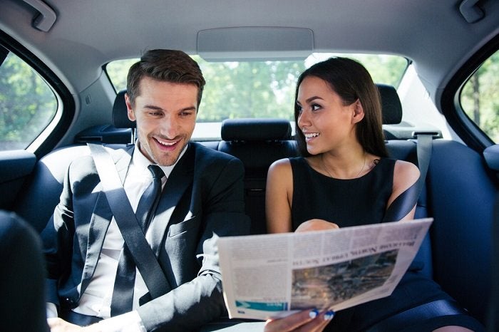 Image of a couple reading a newspaper in the back seat of a car.