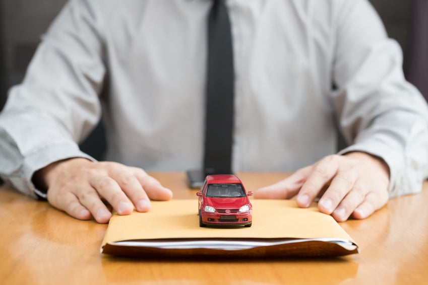 Image of a man with a tie sitting at a table with a manilla folder and a red toy car.